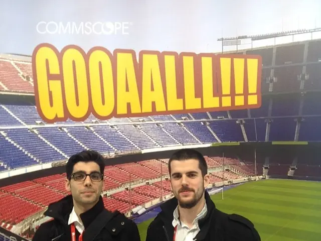 In this picture there are two persons standing. At the back there is a picture of a stadium and...